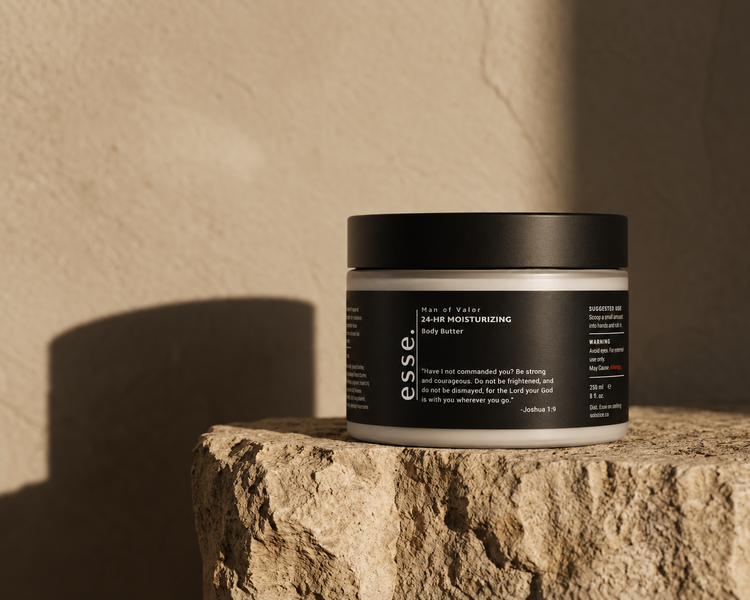 A black jar of esse. Man of Valor 24-hour moisturizing body butter resting on rough stone in warm sunlight